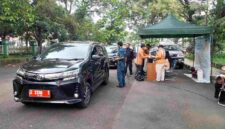Kendaraan plat merah tengah diperiksa uji emisi oleh petugas.