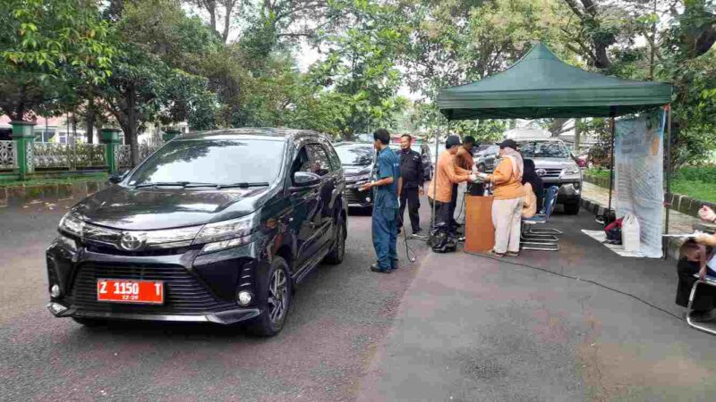 Kendaraan plat merah tengah diperiksa uji emisi oleh petugas.