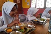 Siswi SDN 1 Kutawaringin tengah menyantap MBG dengan wajah gembira.